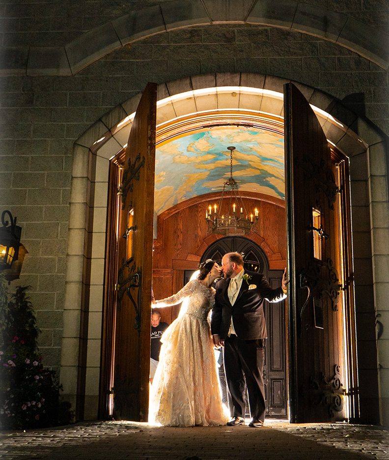 Couple sharing a kiss in the open doorway of a historic stone venue at night